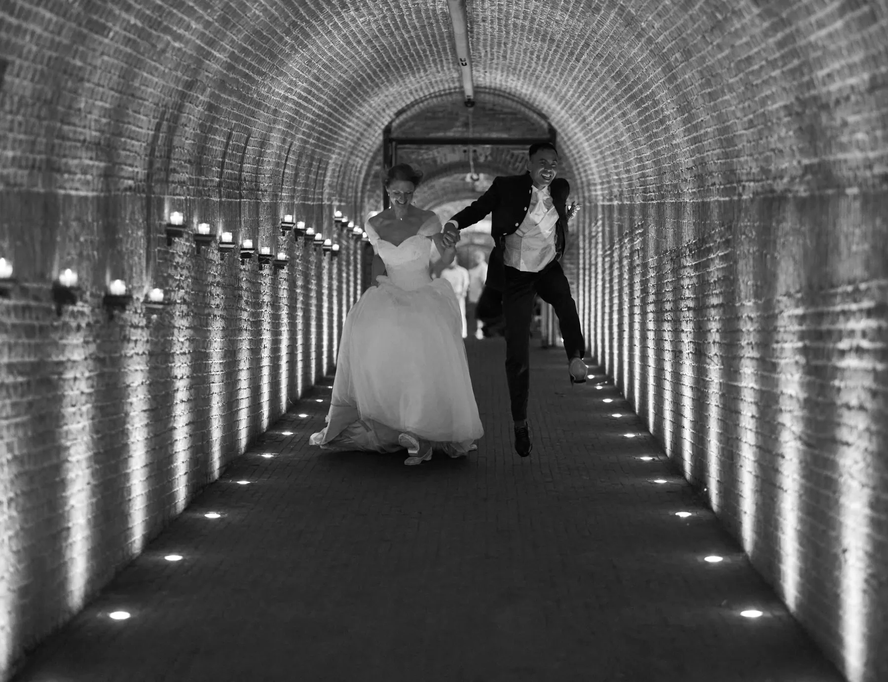 Bruidspaar rent lachend door een verlichte tunnel